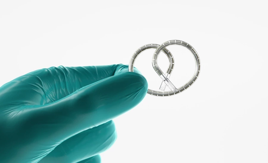 Gloved hand holding a small, pretzel-shaped medical device.