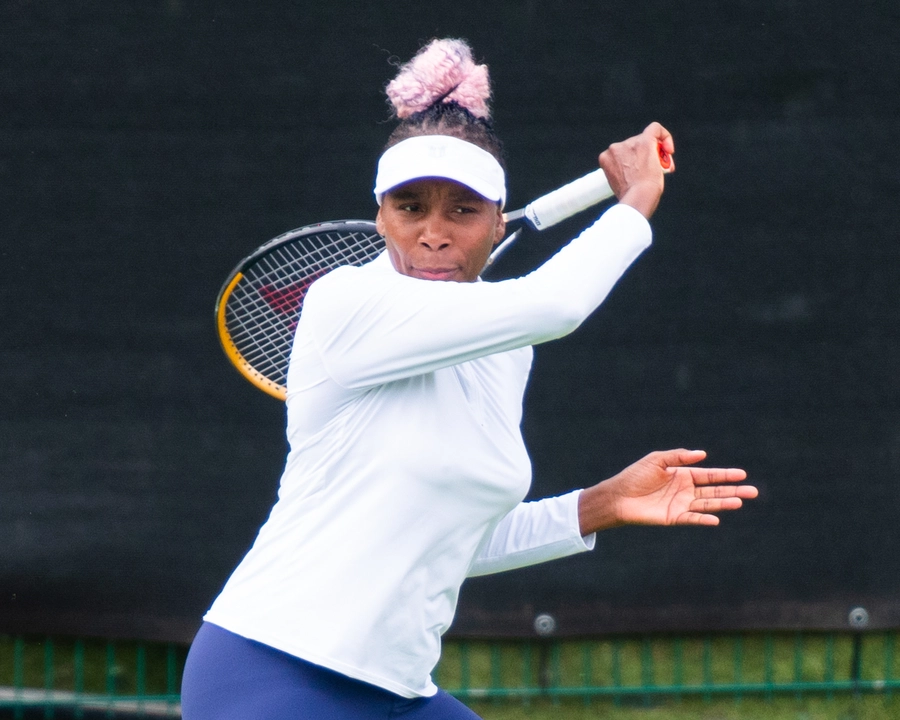 Venus Williams wearing a white long-sleeve shirt and visor, preparing to hit a tennis ball with a racquet during a match.