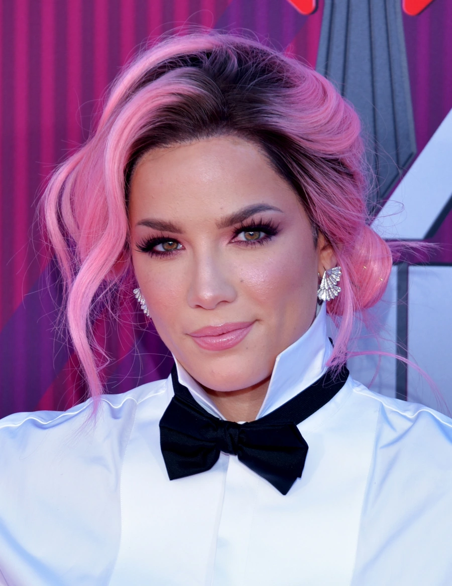 Halsey with styled pink hair, wearing a white collared shirt, black bow tie, and statement earrings.