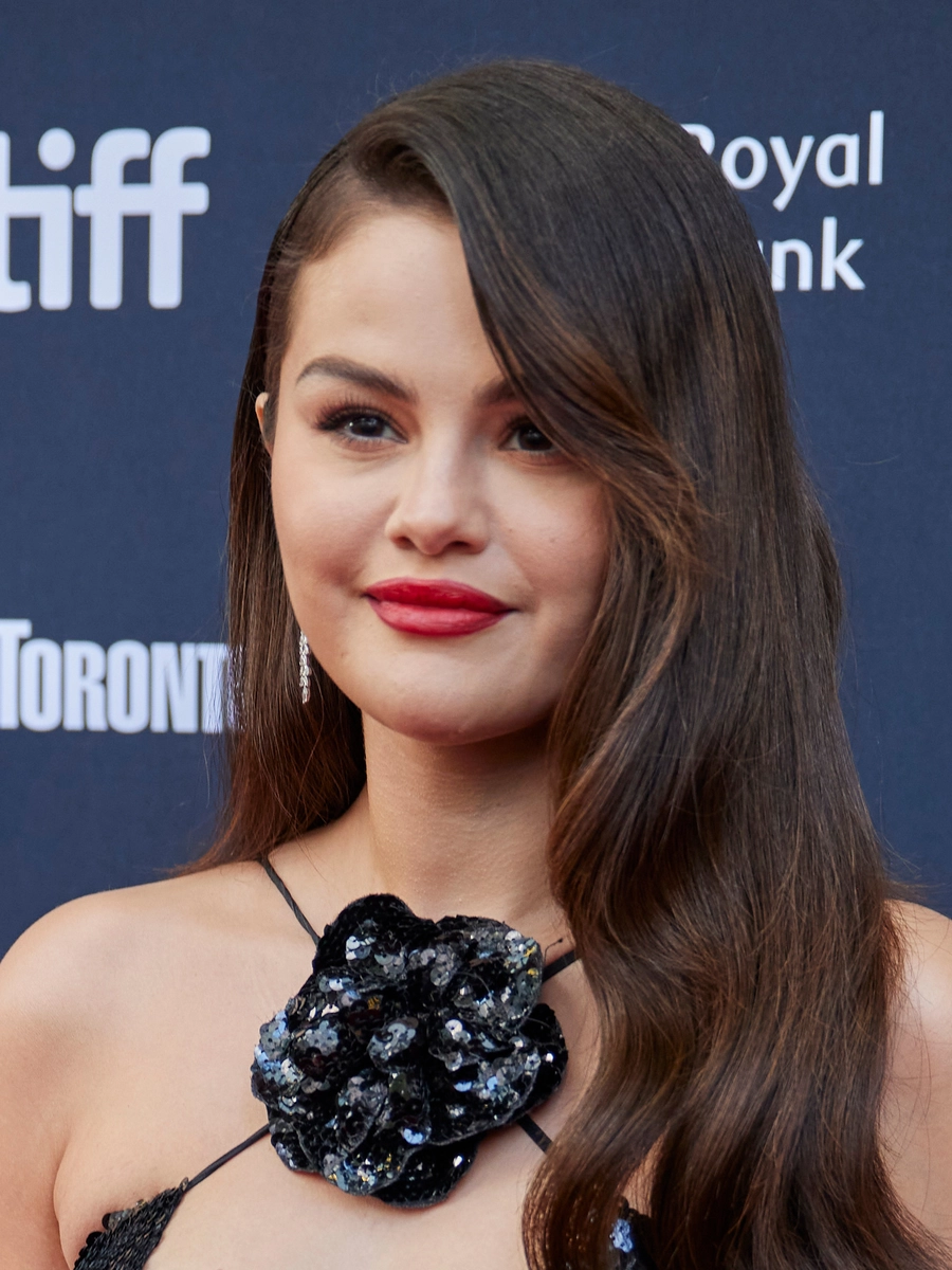 Selena Gomez wearing red lipstick and a black dress adorned with a large, sequined floral detail.